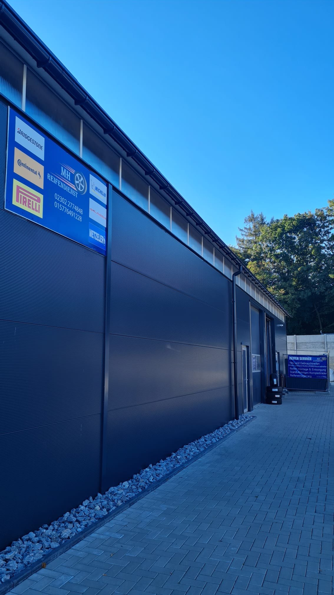 Dunkle Hallenwand von MH Reifendienst mit blauem Markenschild: Bridgestone, Continental, Pirelli, Michelin, Lassa und Metzeler
